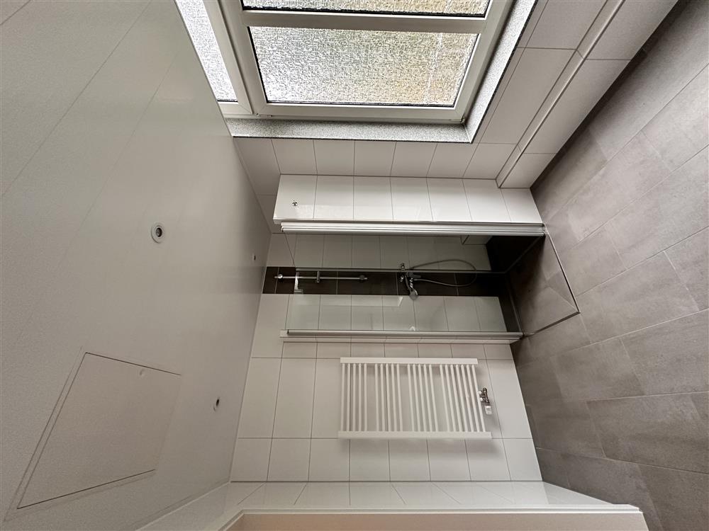 Moderner Badezimmerraum mit begehbarer Dusche, großen Fenstern und weißen Wandfliesen.