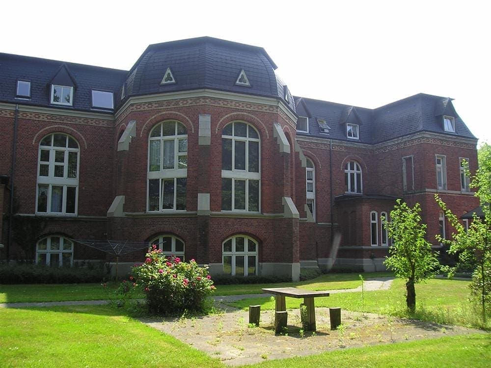Historisches Mehrfamilienhaus der GSG Wohnungsbaugesellschaft Delmenhorst mbH mit rotem Backstein und rundem Erker, umgeben von gepflegtem Garten und Bäumen, im sonnigen, grünen Stadtteil.